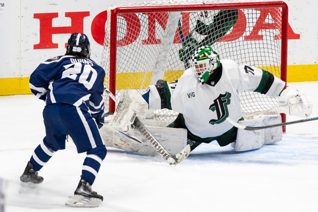 A hockey goalie makes a save off of his arm with a large Honda Center ad behind him