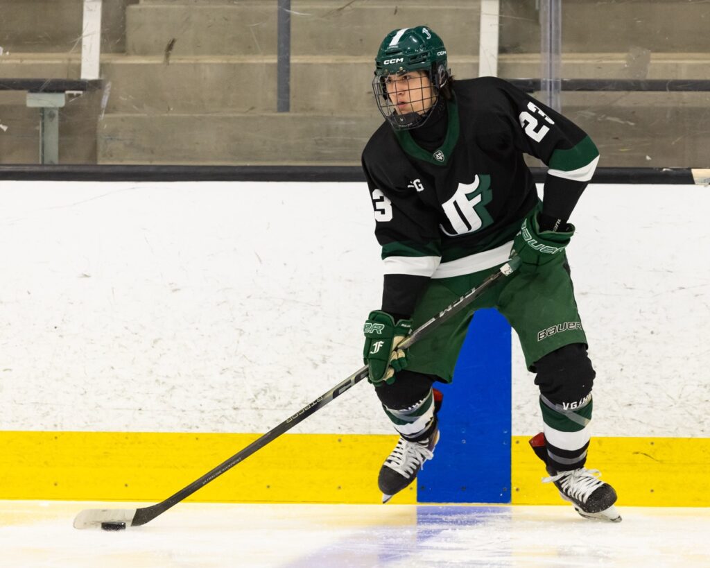 an ice hockey player prepares to pass the puck as he straddles the blue line