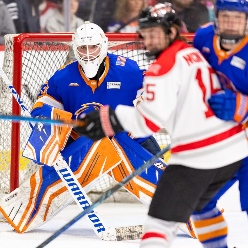 A hockey goalie looks through traffic to track the puck.