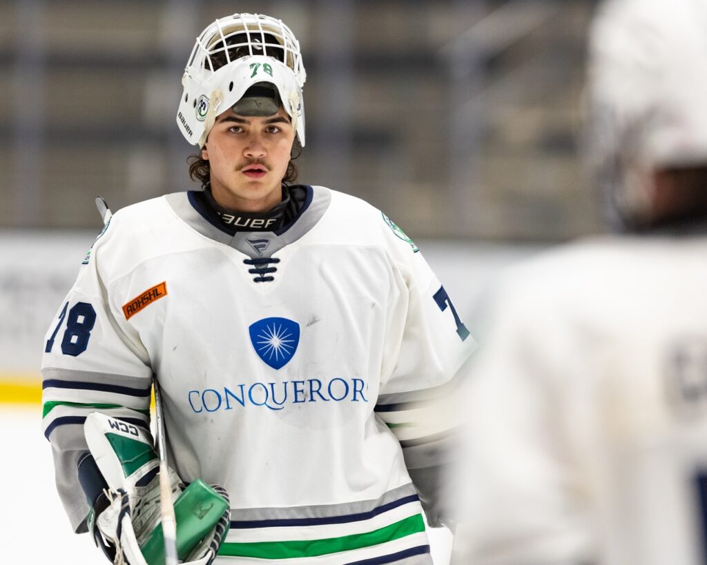 a hockey goalie skates with his mask up toward the bench