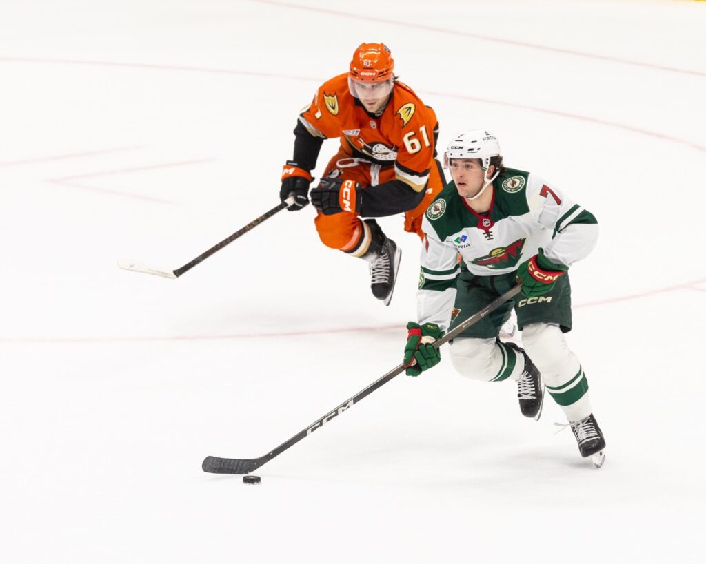 Brock Faber of the Minnesota Wild skates with the puck as Cutter Gauthier of the Anaheim Ducks pursues during an NHL game at Honda Center.