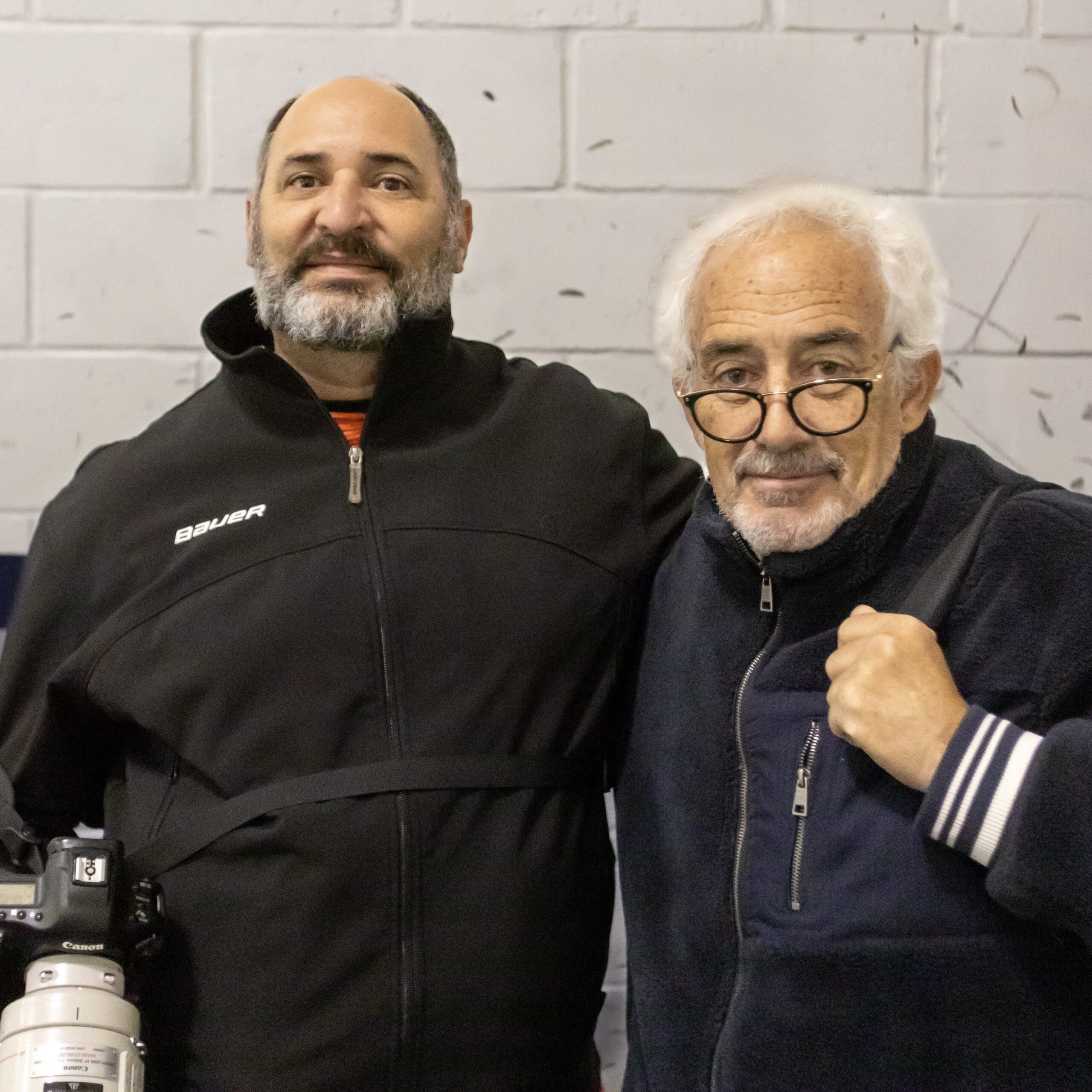 two men pose for a photo while holding cameras. One is hall of fame hockey photographer Bruce Bennett